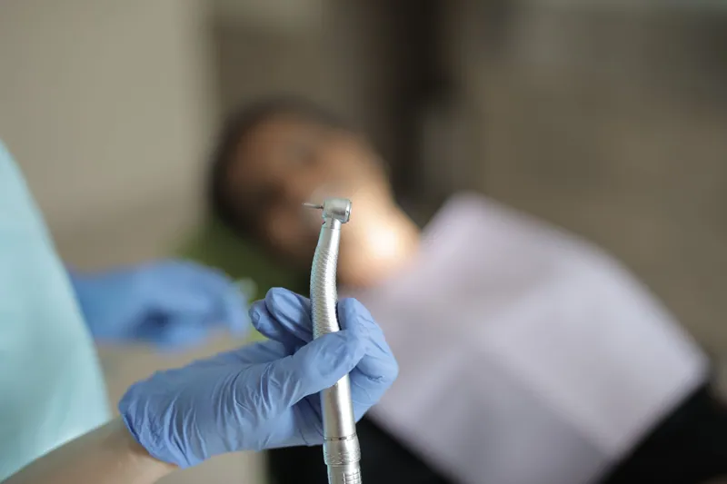 Dentist holding a high-speed handpiece beside a patient in the chair