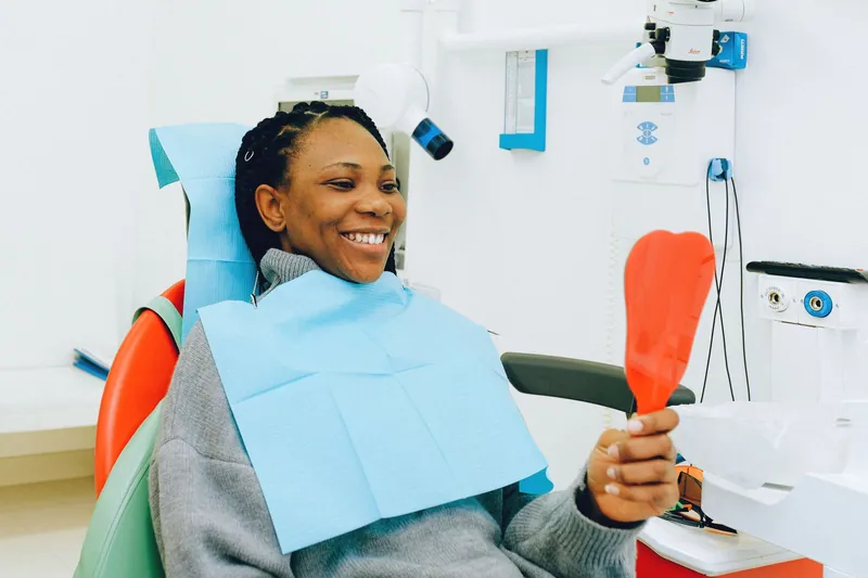 Smiling patient checking her teeth in a hand mirror at the dentist