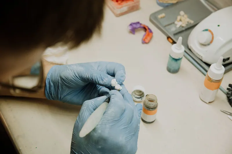 Gloved technician shaping a restoration at a lab bench